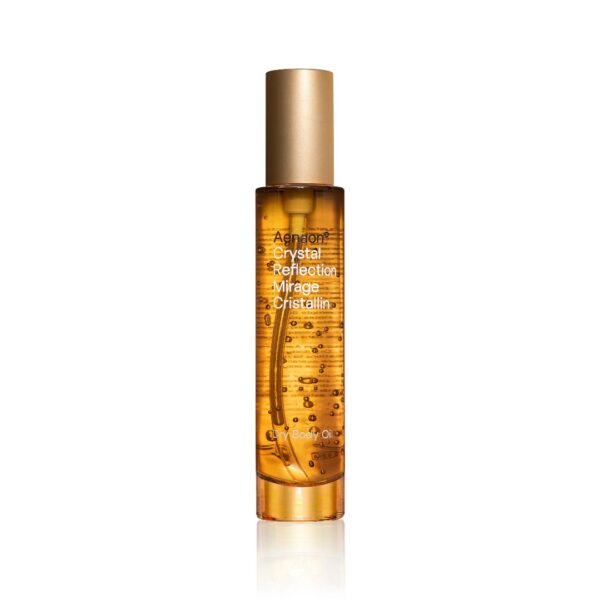 A 100ml bottle of Aenaon Crystal Reflection dry body oil showcasing luxury skincare. The transparent glass bottle with a golden cap emphasizes the premium quality of the golden colored of jojoba and almond oil of this natural organic cosmetic, ideal for organic skincare enthusiasts seeking the best natural and luxury cosmetics.