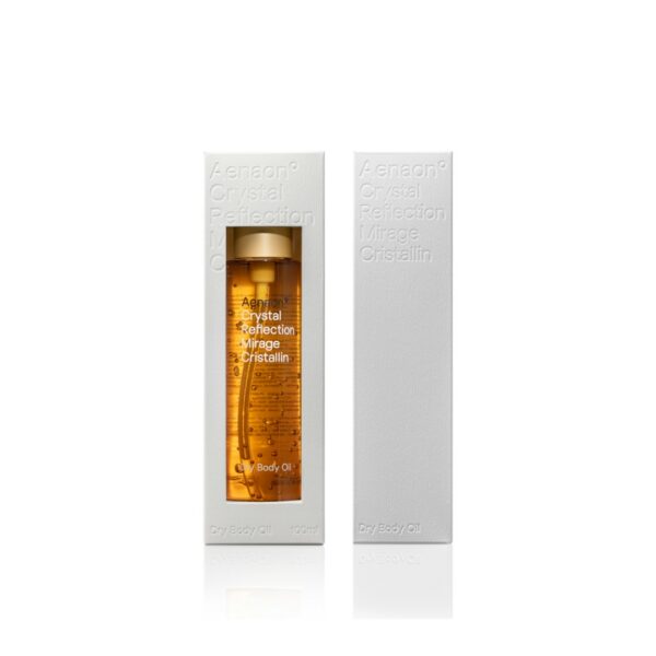 A 100ml bottle of Aenaon Crystal Reflection dry body oil displayed in elegant white packaging, showcasing luxury skincare. The transparent glass bottle with a golden cap emphasizes the premium quality of the golden colored of jojoba and almond oil of this natural organic cosmetic, ideal for organic skincare enthusiasts seeking the best natural and luxury cosmetics.